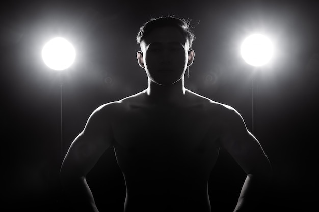 Muskulöser Eignungsmann übt gesunden Lebensstil im dunklen Hintergrundschattenbildrücklicht aus