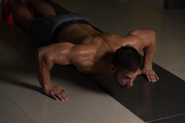 Foto muskulöser erwachsener athlet, der liegestütze als teil des bodybuilding-trainings macht