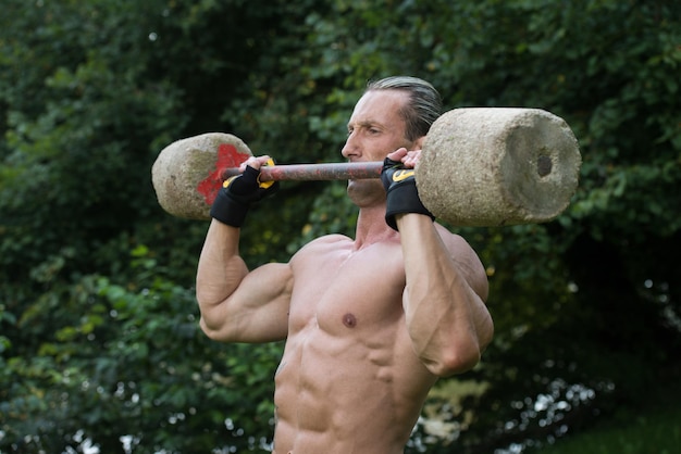 Foto muskulöser erwachsener mann, der eine übung für die schultern mit gemachtem handhantel-training im freien macht