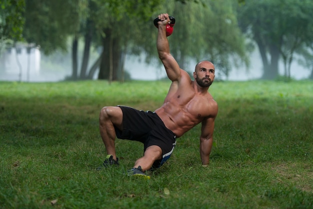 Muskulöser Fitness-Mann balanciert Kettlebells mit einer Hand im Freien