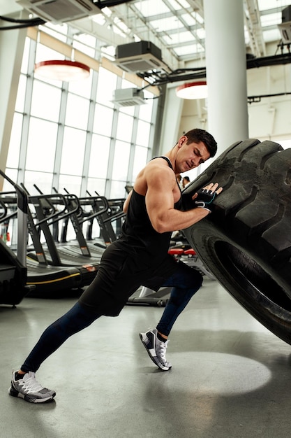 Muskulöser Fitness-Mann, der große Reifen im Fitness-Center-Konzept bewegt, um Trainingstraining zu heben