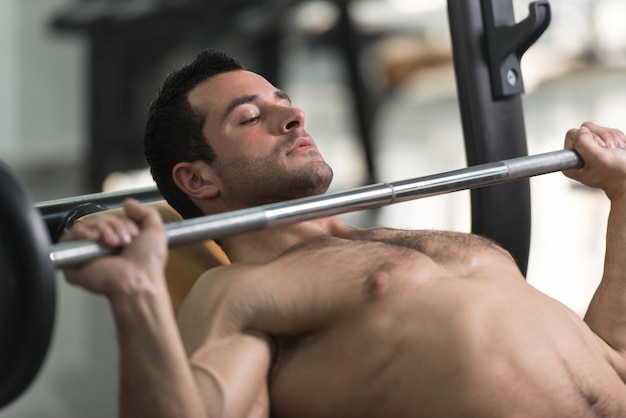 Muskulöser haariger Mann, der im Fitnessstudio schwere Übungen für die Brust mit Langhantel macht