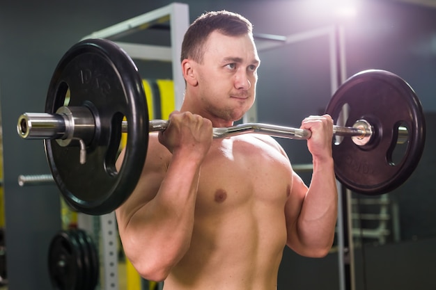 Muskulöser junger Mann, der Gewichte im Fitnessstudio hebt.