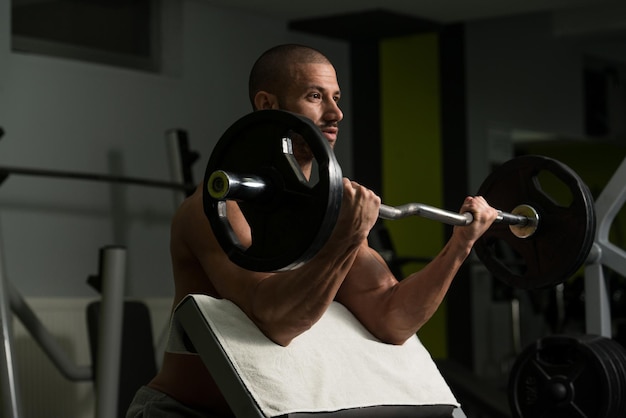 Muskulöser junger Mann, der im Fitnessstudio schwere Übungen für den Bizeps macht