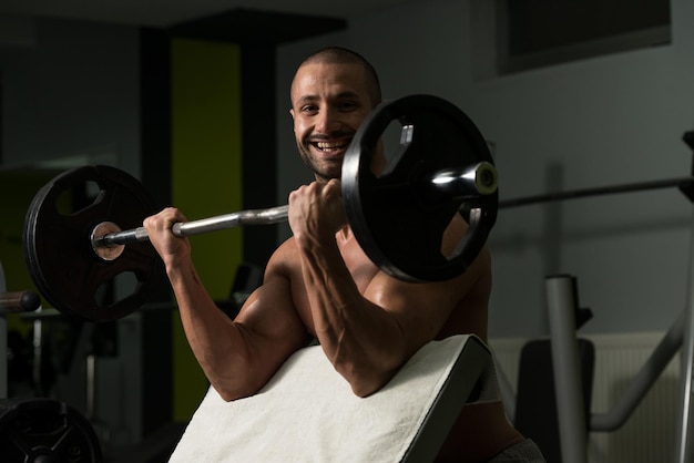 Muskulöser junger Mann, der im Fitnessstudio schwere Übungen für den Bizeps macht