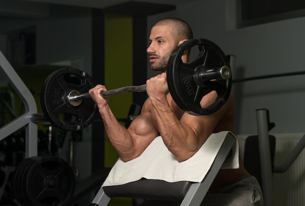 Muskulöser junger Mann, der im Fitnessstudio schwere Übungen für den Bizeps macht