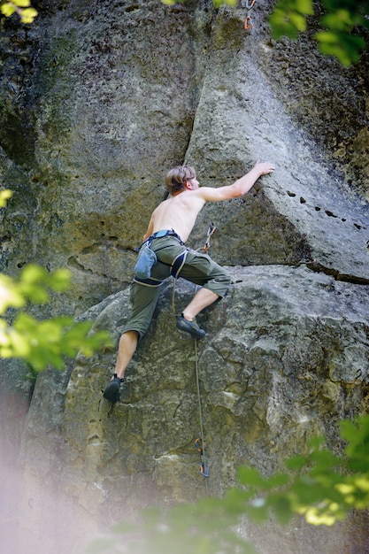 Muskulöser Kletterer klettert auf Klippenwand mit Seil