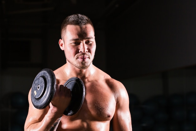 Muskulöser Mann, der im Fitnessstudio trainiert, das Übungen mit Hanteln am Bizeps macht, starker männlicher nackter Torso