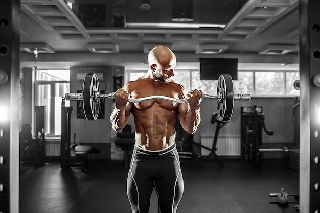 Muskulöser Mann, der im Fitnessstudio trainiert, das Übungen mit Hanteln macht