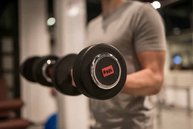 Muskulöser Mann, der mit roter Hantel im Fitnessstudio trainiert