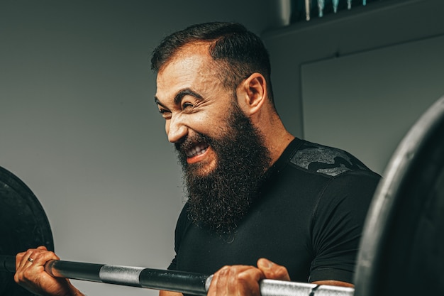 Muskulöser Mann in der schwarzen Sportbekleidung, die Langhantel in einem Fitnessstudio hebt