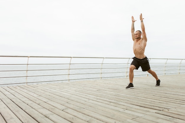 Muskulöser Mann mit nacktem Oberkörper praktiziert Hatha-Yoga und balanciert Pose am Strand. Gesundes Lebensstilkonzept