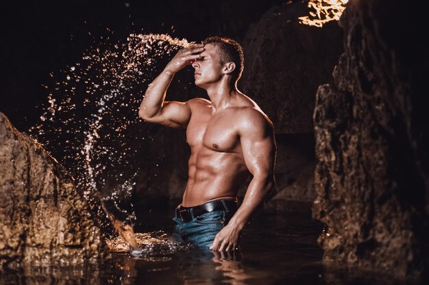 Muskulöser Mann ohne Hemd spritzt Wasser und steht gegen eine Felsformation