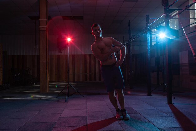 Muskulöser Mann trainiert mit dem TRX-System in einem dunklen Fitnessstudio Athlet mit nacktem Oberkörper Training mit Widerstandsbändern in rotblauem Neonlicht Funktionelles Crosstraining