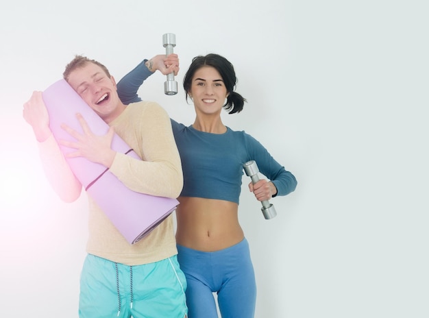 Muskulöser Mann und Mädchen im Fitnessstudio mit Hanteln und Matte