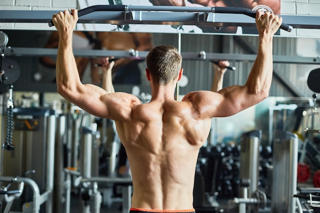 Muskulöser nackter Rücken des gutaussehenden Mannes, der im Fitnessstudio trainiert