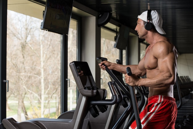 Muskulöser reifer Mann beim Aerobic Elliptical Walker im modernen Fitnesscenter