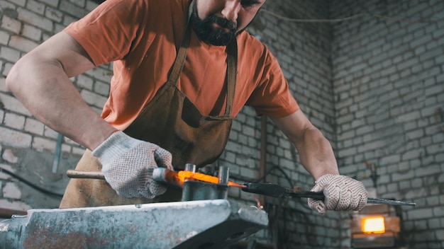 Muskulöser Schmied in der Schmiede, die Stahlprodukte hämmert, Kleinunternehmen