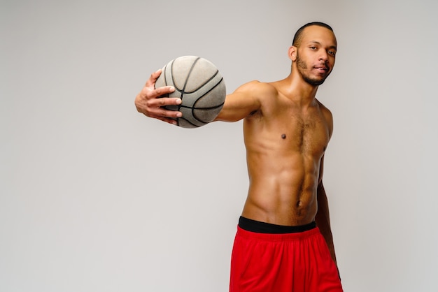 Muskulöser Sportler, der scheißlos über hellgrauer Wand Basketball spielt