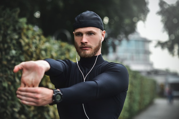 Muskulöser Sportler, der sich vor einem Sporttraining auf der Straße im Stadtpark ausstreckt