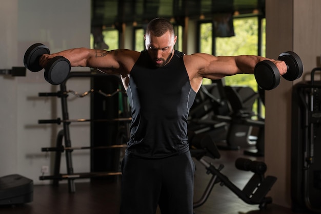 Muskulöses männliches Modell, das Schultern mit Hanteln trainiert