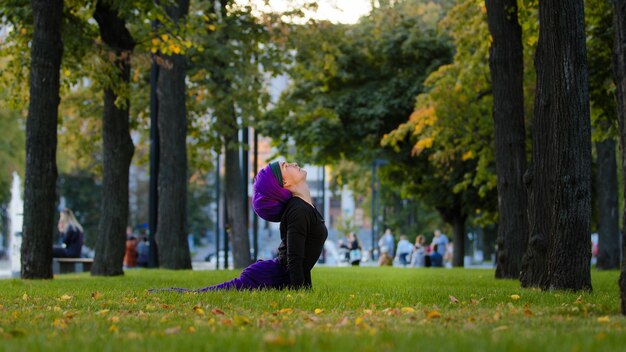 Muslimisch-islamische Frau praktiziert Yoga-Sonnengruß im Park auf Gras. Morgenroutine mit Blick auf den Hund