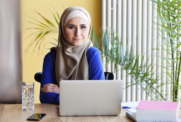 Muslimische Asiatin, die im Büro mit Laptop arbeitet