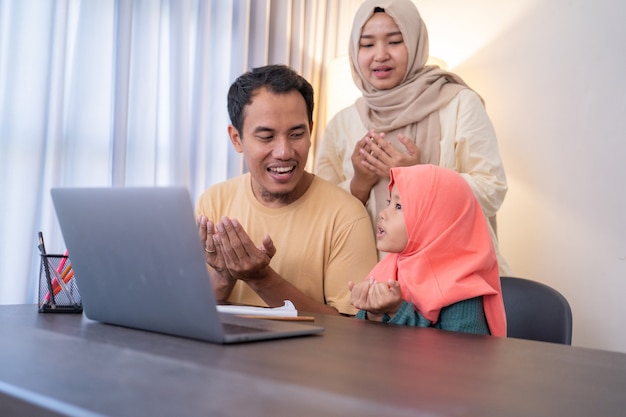 Muslimische Eltern und Tochter beten zusammen, während sie zu Hause einen Laptop benutzen