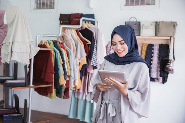 Muslimische Frau, die digitales Tablett im Bekleidungsgeschäft verwendet