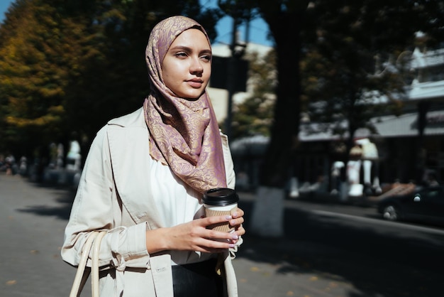 Muslimische Frau geht die Straße entlang und hält einen Pappbecher mit Kaffee in der Hand