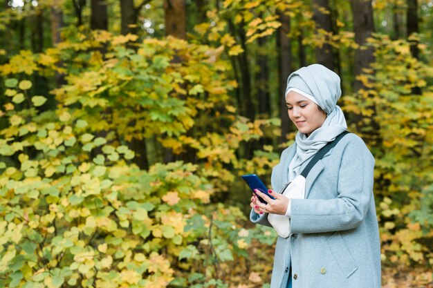 Muslimische Frau im Park mit Smartphone verbunden online drahtlos. Platz kopieren