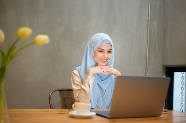 Muslimische Frau mit Hijab arbeitet mit Laptop im Café