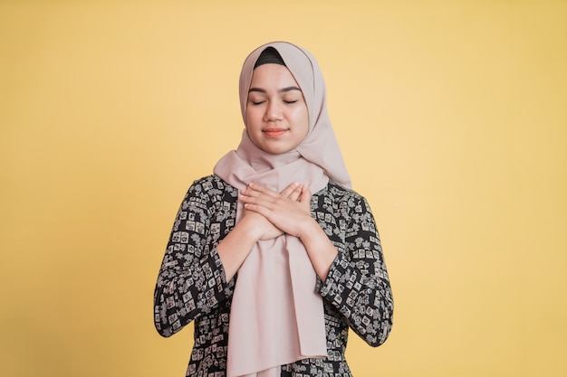 Muslimische Frau mit Hijab, die Brust und Augen mit geduldigem Ausdruck geschlossen hält
