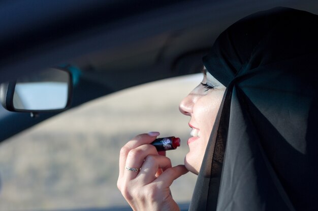 Muslimische Frau mit Lippenstift in einem Auto, traditionelle Kleidung.