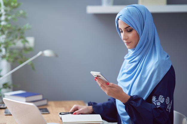 Muslimische Frau mit Smartphone im Büro