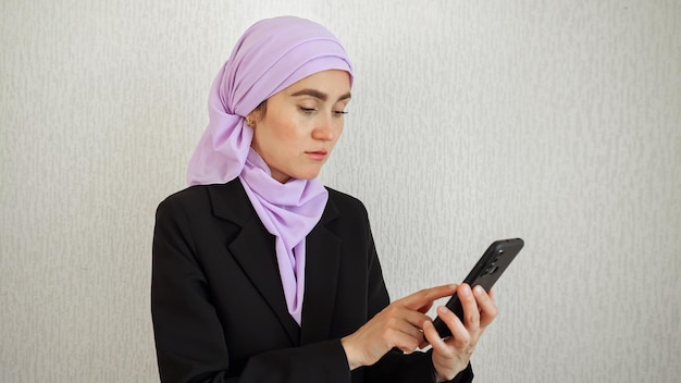 Muslimische Frau scrollt im Internetbrowser auf schwarzem Smartphone durch den Newsfeed. Dame im rosafarbenen Hijab liest Nachrichten von Freunden in sozialen Medien