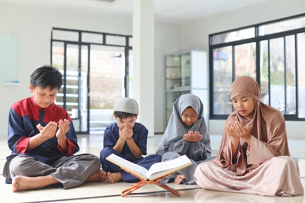 Muslimische Kinder heben die Hände, um nach oder vor dem Zusammenlesen des Koran in der Moschee zu beten