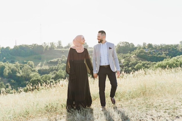 Muslimische Liebesgeschichte eines gemischten Paares. Mann und Frau lächeln und gehen auf den grünen Hügeln.