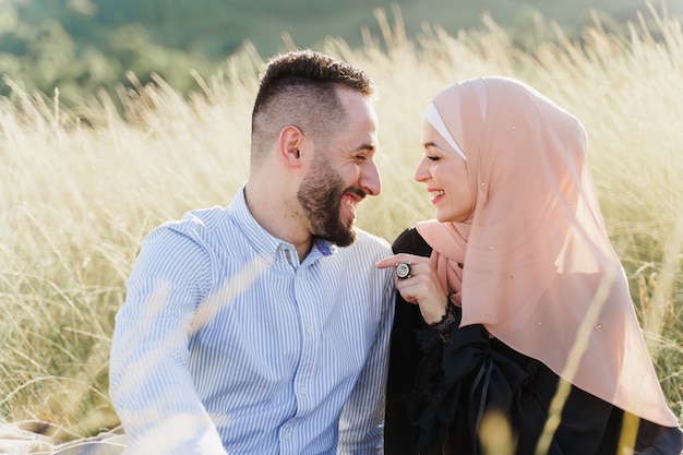 Muslimische Liebesgeschichte. Gemischte Pärchensitze im Gras, Lächeln und Umarmungen