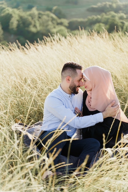 Muslimische Liebesgeschichte. Gemischte Pärchensitze im Gras, Lächeln und Umarmungen