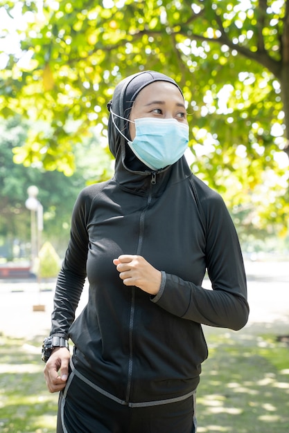 Muslimische Sportfrau tragen Maske, die im Freien in der Parkübung läuft