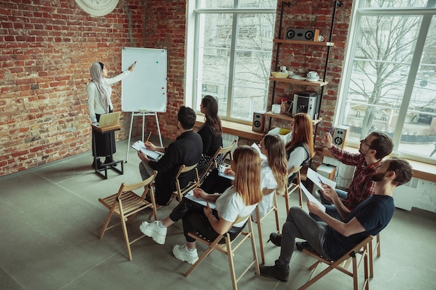 Muslimische Sprecherin, die Präsentation in der Halle beim Workshop hält. Publikum oder Saal. Erhöhte Ansicht der Teilnehmer im Publikum. Konferenzveranstaltung, Schulung. Bildung, Vielfalt, inklusives Konzept.