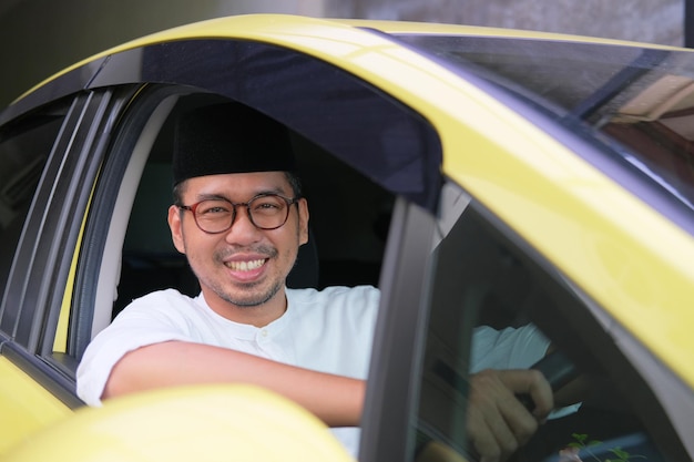 Muslimischer asiatischer Mann, der beim Autofahren in die Kamera lächelt