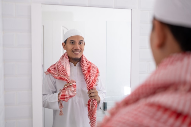 Muslimischer asiatischer Mann, der Spiegel betrachtet und sich anzieht, bevor er zur Moschee geht