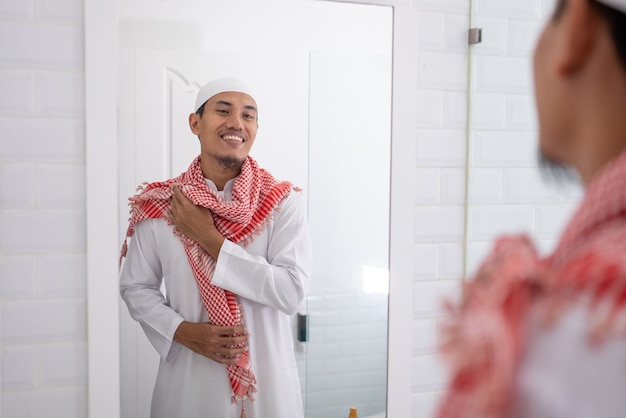 Muslimischer asiatischer Mann, der Spiegel betrachtet und sich anzieht, bevor er zur Moschee geht
