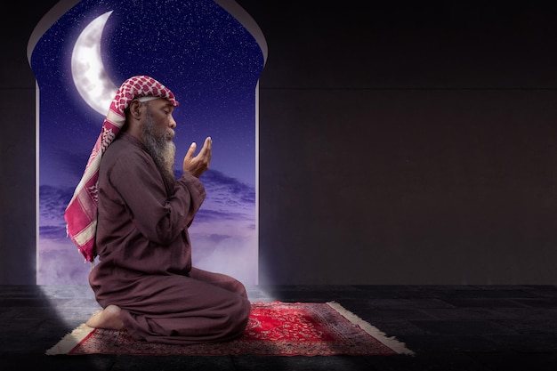 Muslimischer Mann mit Bart, der Keffiyeh mit Agal beim Beten trägt, während er die Hände erhebt