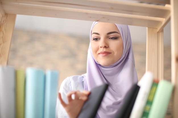 Muslimischer Student, der Buch aus dem Regal in der Bibliothek auswählt