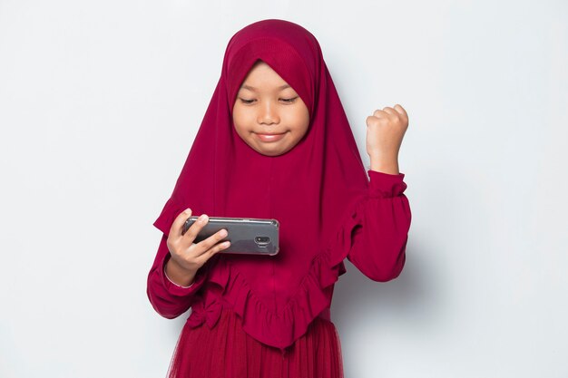 Muslimisches asiatisches kleines Mädchen mit Smartphone-Spiel auf weißem Hintergrund