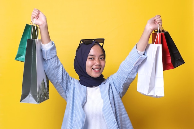 Muslimisches Mädchen im lässigen Stil hebt die Arme und zeigt bunte Papiertüten