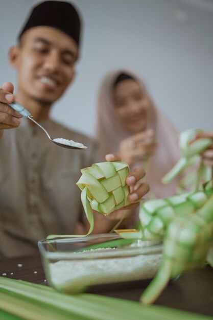 Muslimisches paar asiatisch, das zu hause ketupat-reiskuchen mit palmblatt macht